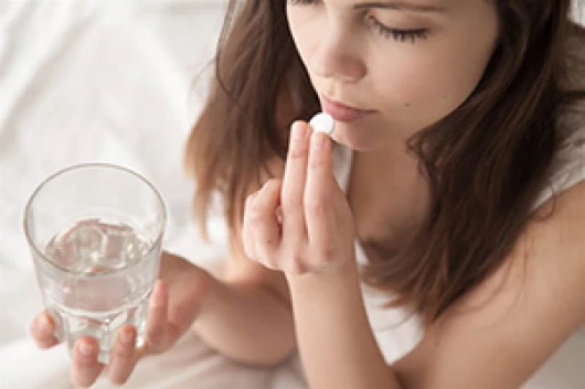 Woman holding glass of water and a pill by her mouth